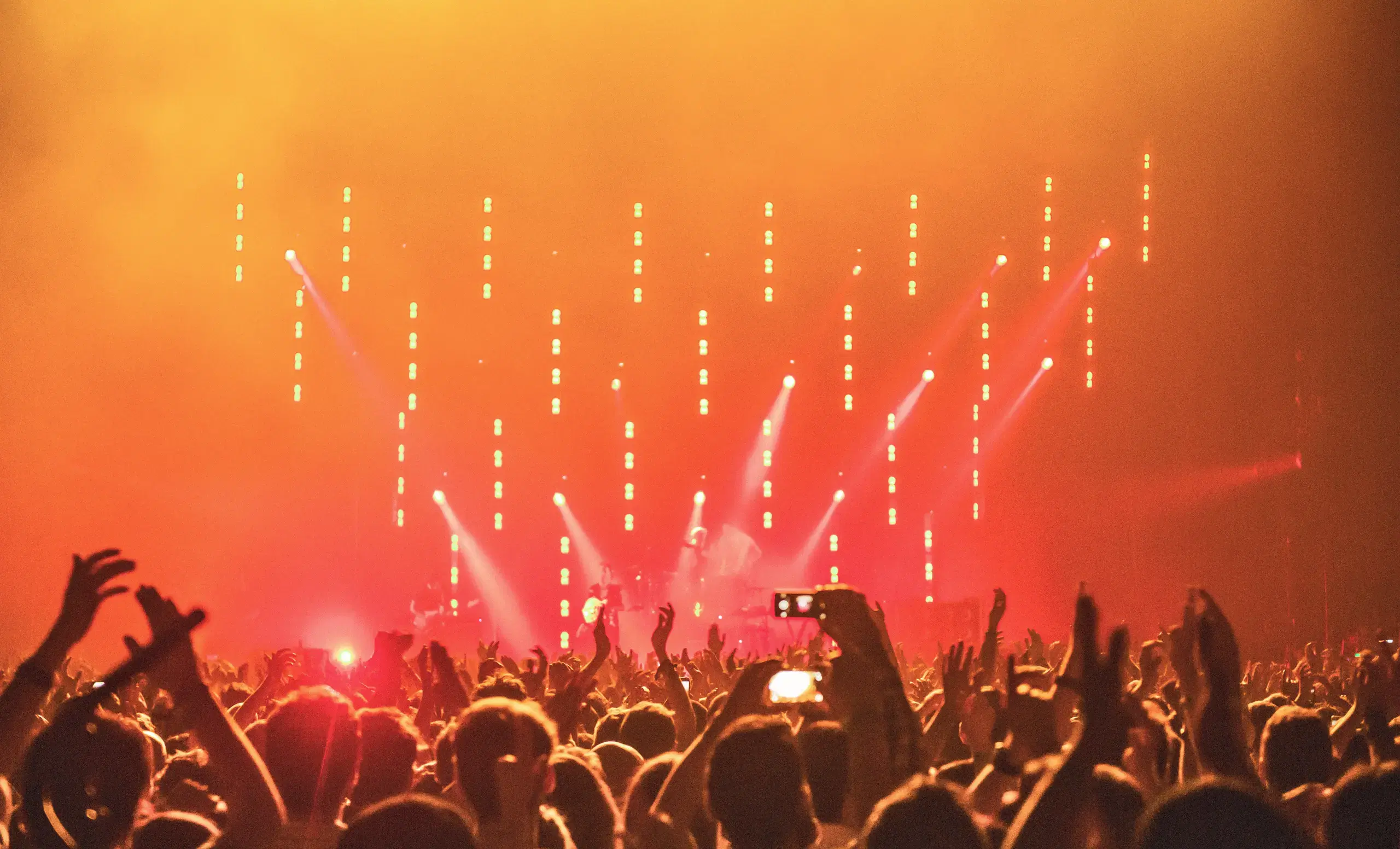 Crowd photo of a concert facing a performing band on stage with orange and red lights
