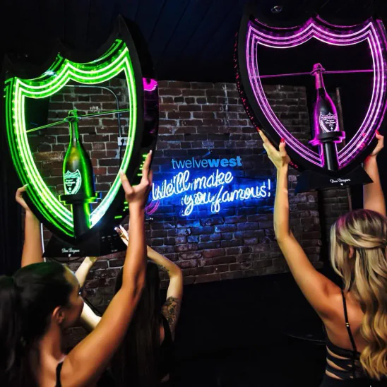 Two bottle servers each holding a green and pink glowing presenter and bottle of Dom Perignon Luminous (left) and Dom Perignon Luminous Rose (right) respectively